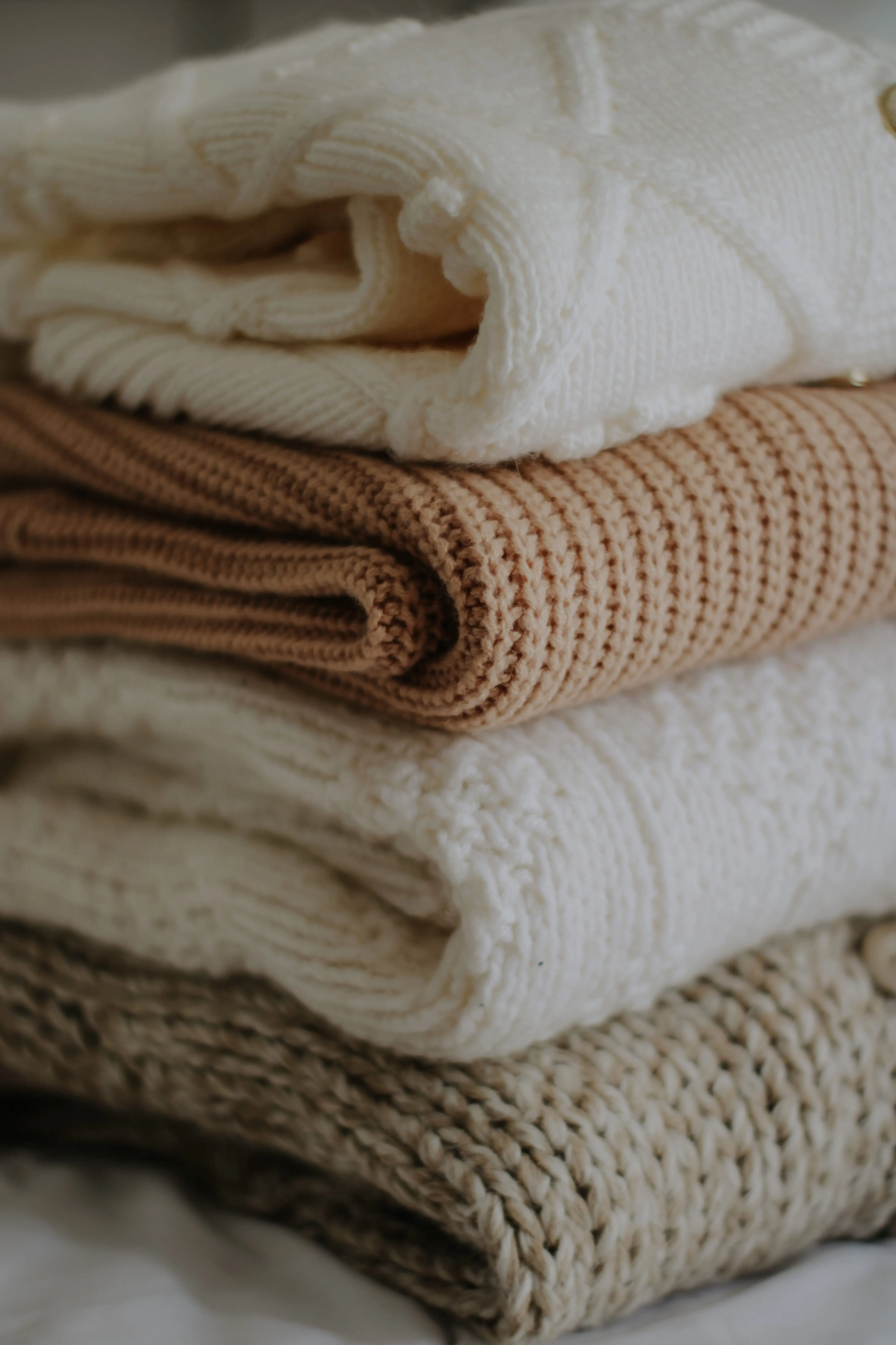 Capsule wardrobe knitwear essentials — stacked cream, camel and beige knit sweaters