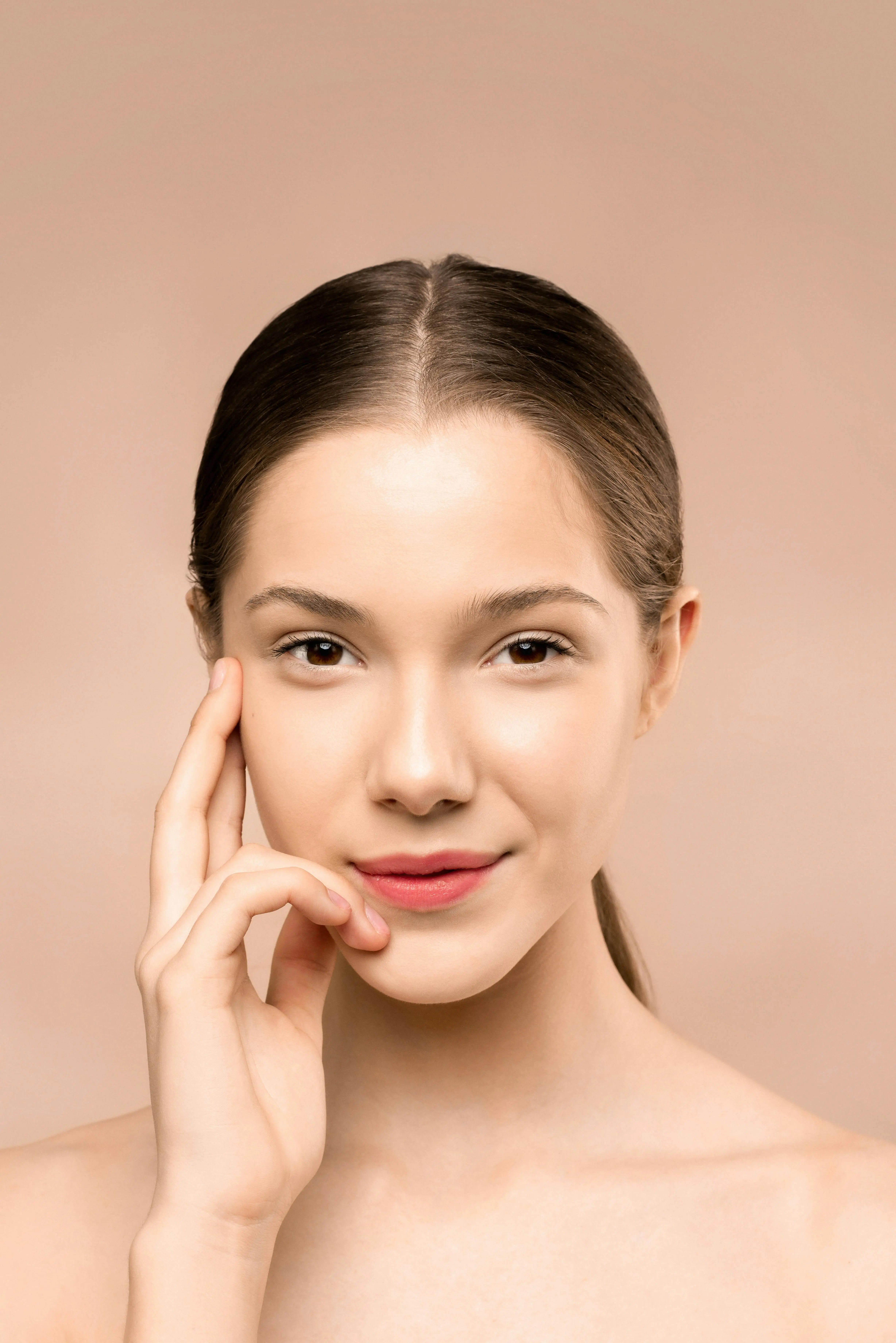Glass skin glowing complexion — woman with radiant even-toned skin warm beige background