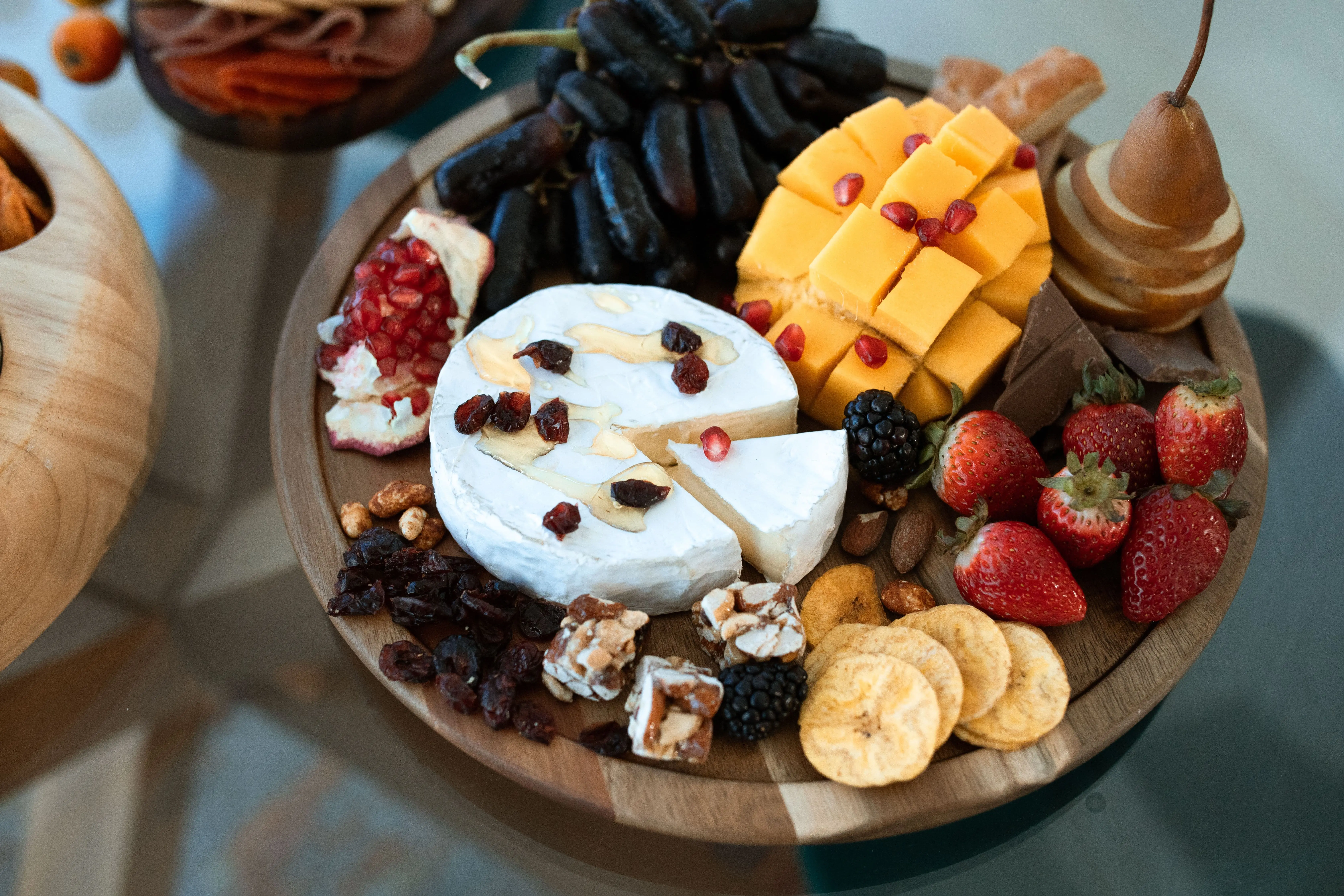 Beautiful round grazing board with brie, cheddar, honey dipper, grapes and strawberries