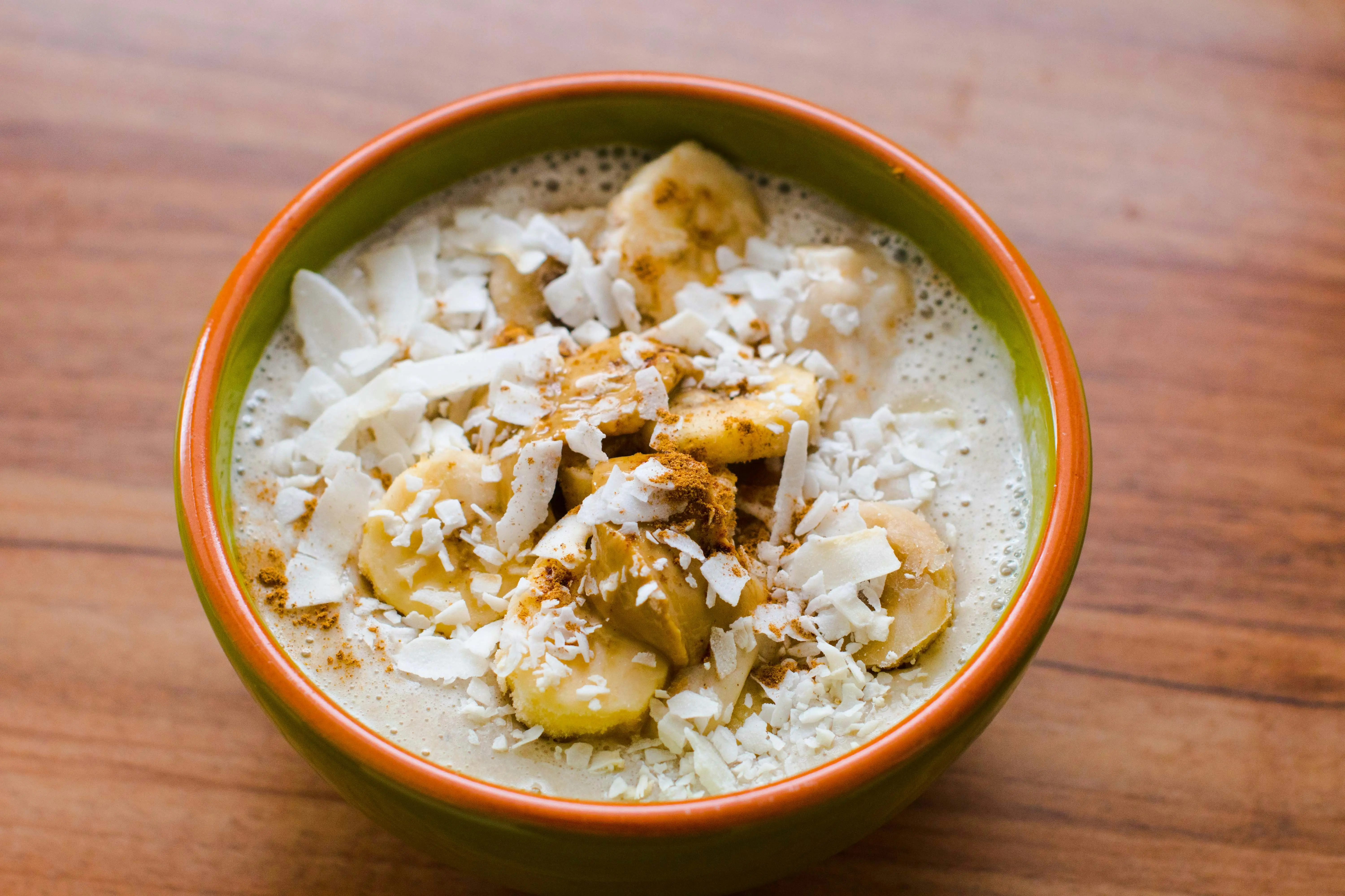 Banana smoothie bowl with coconut flakes and cinnamon on a wooden surface, wholesome high-protein breakfast ingredients, warm natural light