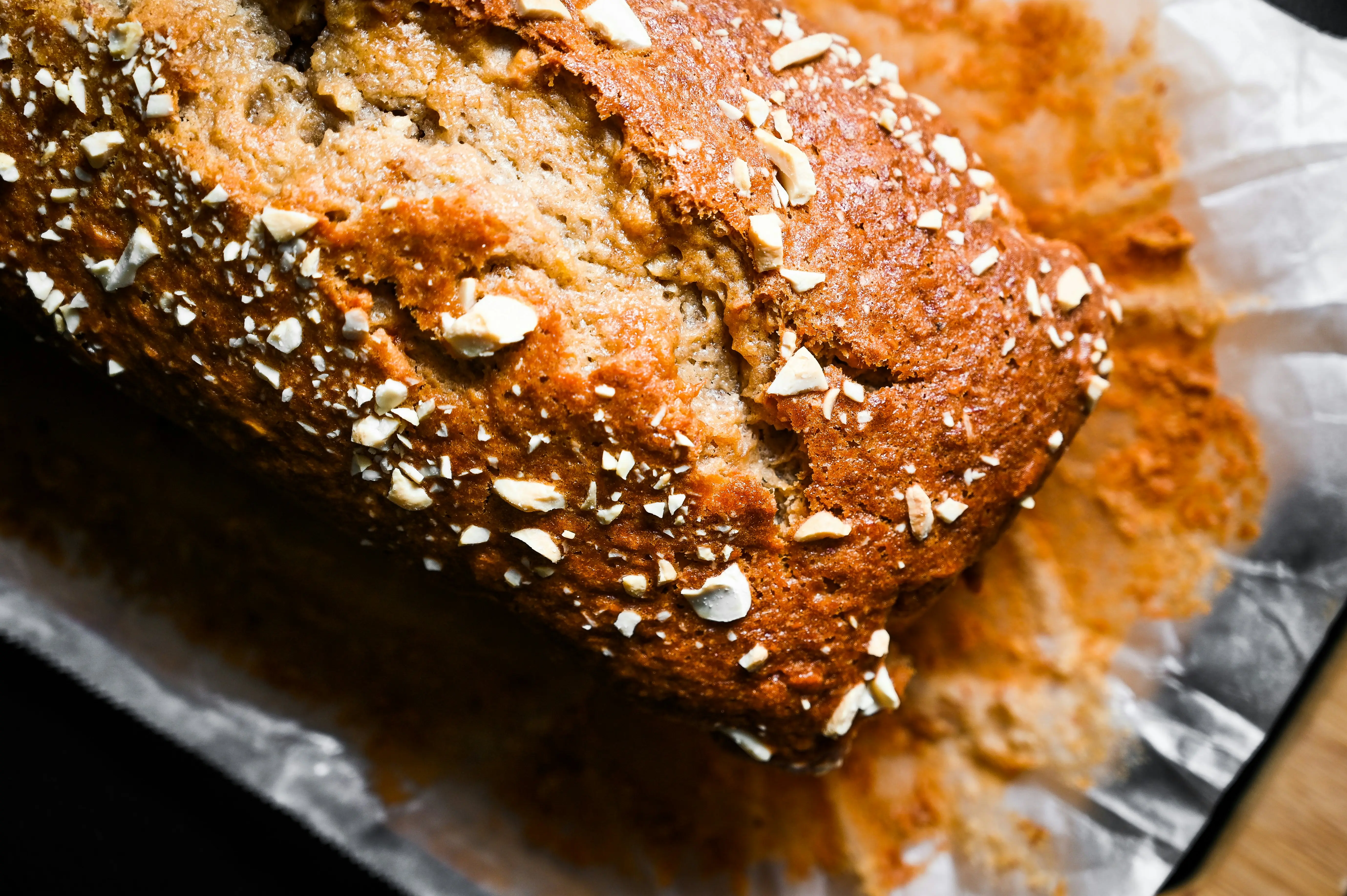 Close-up of banana bread loaf topped with chopped walnuts on parchment paper, golden brown crust with visible texture