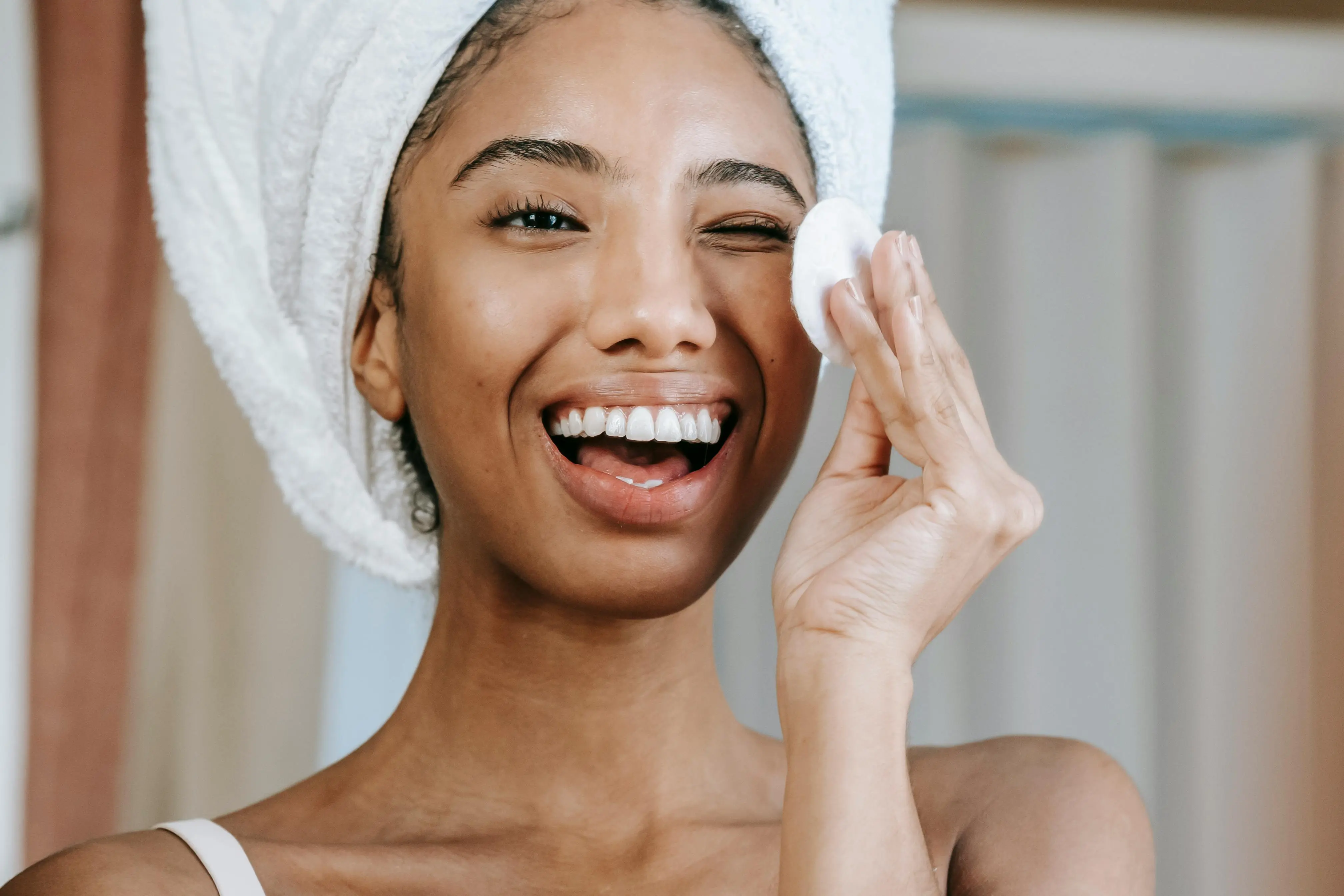 Skincare cleansing routine glass skin — woman applying cotton pad with towel wrap glowing skin